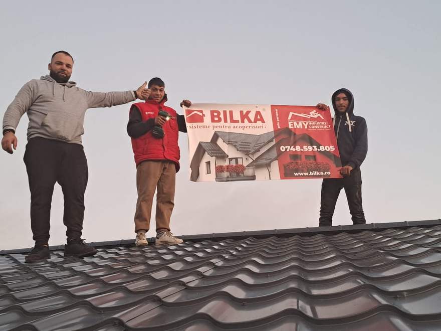 Echipa pe acoperișul finalizat al casei Manea, cu bannerul partenerilor Bilka și Emy Industry Construct